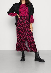 Figurformad långärmad rosa blus med svart hjärt-mönster, parat med en svart kjol som har ett liknande hjärt-design och en sidöppning, bärs tillsammans med svarta stövlar.