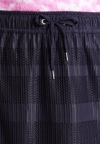 Jupe plissée marine avec taille élastique et cordon de serrage. Présente des rayures horizontales texturées et des accents métalliques aux extrémités du cordon.