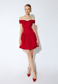 Robe rouge décolletée avec un corsage ajusté et une jupe évasée, confectionnée dans un tissu lisse. Assortie à des chaussures à talons rouges.