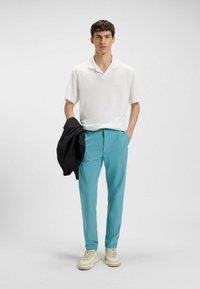 Biała koszulka polo, turkusowe spodnie, czarna kurtka zarzucona na rękę, jasne sneakersy, minimalistyczny design, gładki materiał, bez widocznych wzorów.