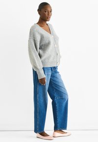 Light gray cardigan with a v-neck, large buttons, and a soft texture, paired with loose blue jeans and light pink flats.