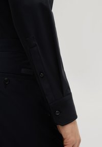 Schwarzes Langarmshirt mit taillierter Passform. Mit gepolsterten Manschetten und einem kleinen Logostick auf der Seite. Glattes, leichtes Material.