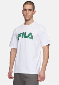 Camiseta de algodón blanca con un gran logo verde de "FILA". Manga corta y diseño de cuello redondo. Textura suave, ajuste relajado.