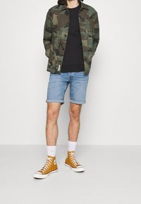 Mekko, musta toppi, farkkuhousut ja sinapinkeltaiset korkeat lenkkarit. Ominaisuuksia ovat napit, käärityt shortsit ja valkoiset nilkkasukat.