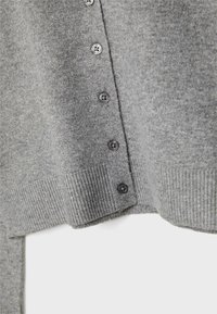Harmaa neulecardigan, jossa on ribattu helma ja kaulus, kuusi tummaa nappia edessä sekä pehmeä rakenne.