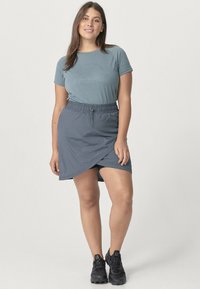 lichtblauw T-shirt met een bedrukte ontwerp, gecombineerd met een donkergrijze wikkelrok. De outfit is compleet met zwarte sportschoenen.