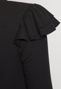 Černý žebrovaný top s detaily ruffles na ramenou. Hladká textura, přiléhavý střih a krátké rukávy zvýrazňují styl.