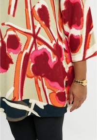 Tunic multicolore con motivi floreali in rosso, rosa e arancione su uno sfondo crema; orlo arrotondato e maniche a metà.