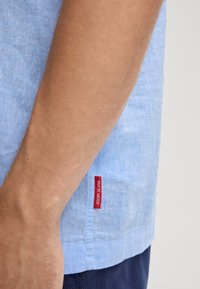 Lichtblauw linnen overhemd met korte mouwen, voorzien van een rode "JOOP! JEANS" label op de zijzoom. Zichtbare textuur en casual ontwerp.