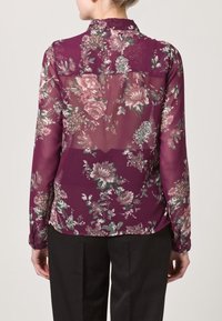 Sheer, purple floral blouse with long sleeves, featuring a collar and back yoke detail, adorned with pink and green patterns on a lightweight fabric.