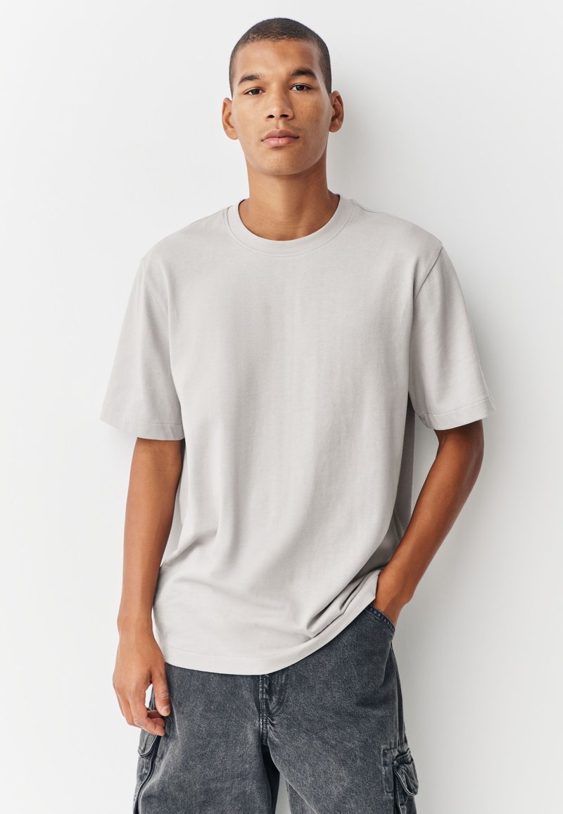 Vaaleanharmaa lyhythihainen t-paita, valmistettu pehmeästä kankaasta, jossa pyöreä kaula-aukko ja rento istuvuus, yhdistetty tummanharmaisiin cargo-shortseihin.