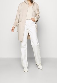 Cardigan in lana beige con tasche anteriori, abbinato a pantaloni bianchi a gamba larga e stivaletti con punta; design semplice e pulito e texture morbida.