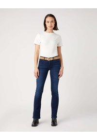 Witte katoenen t-shirt met ronde hals, gecombineerd met donkerblauwe denim jeans met een slim fit en een tan kleurige riem. Zwarte enkellaarsjes maken de outfit compleet.