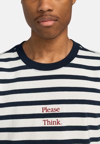 Camiseta de algodón a rayas en azul marino y blanco. Presenta un escote redondo y texto rojo bordado "Por favor, piensa." debajo del área del pecho.