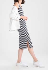 Paski midi sukienka w granatowo-białe, z dekoltem z przodu, noszona z białą dżinsową kurtką i białymi trampkami.