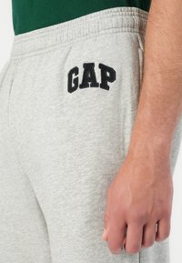 Grå bomullssvetter med elastisk midjebånd og svart brodert "GAP"-logo på venstre lår. Glatt tekstur, avslappet passform.