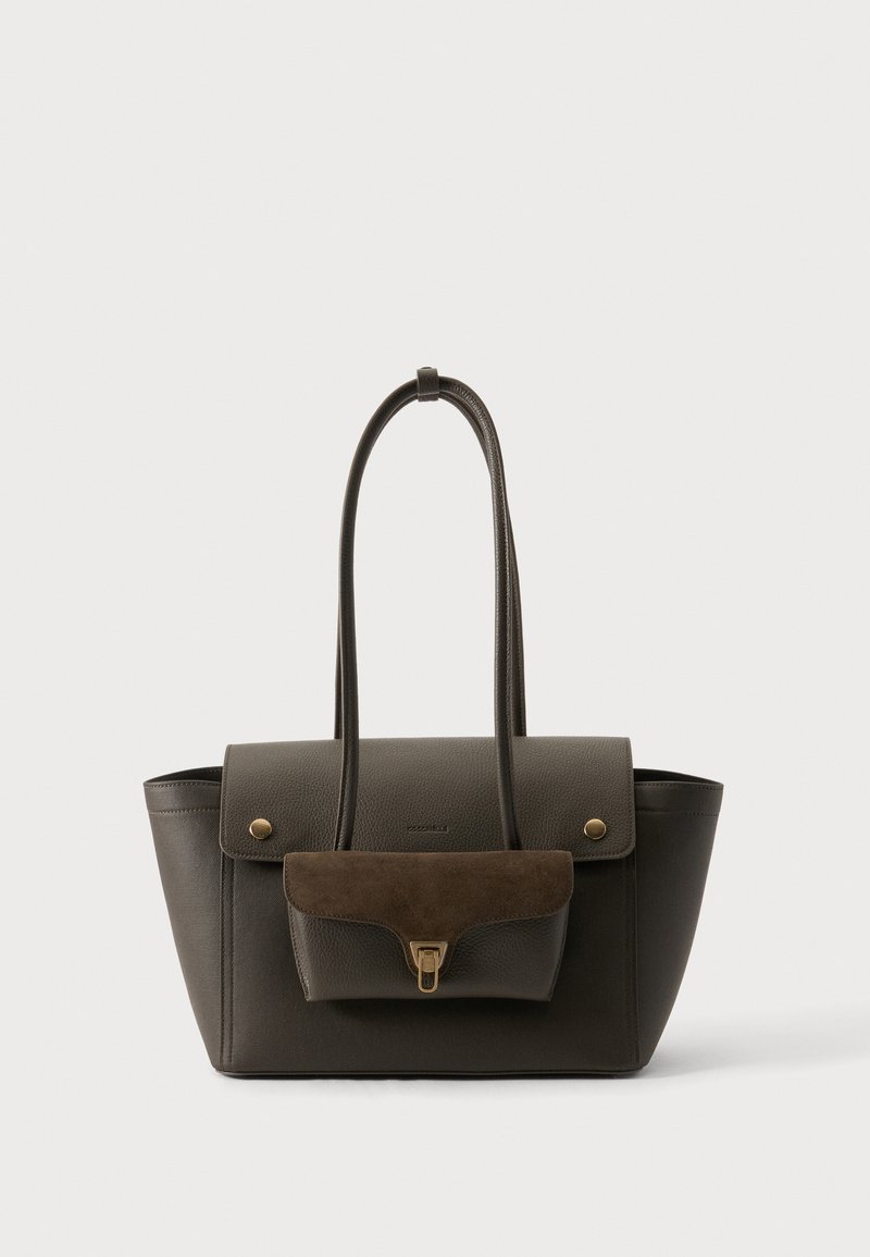 Sac cabas en cuir marron foncé avec poche à rabat présentant un détail en daim et un fermoir doré, deux longues anses sur fond neutre.