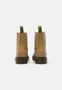 Bottes de cheville en cuir tanné avec une finition texturée, des tirants jaunes et noirs, et des semelles en caoutchouc présentant des coutures visibles et un design épais.