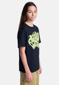 Μαύρο βαμβακερό μπλουζάκι με μεγάλη γραφική απεικόνιση φωτιάς σε νέον πράσινο χρώμα στο μπροστινό μέρος. Βραχίονες κοντοί, στρογγυλή λαιμόκοψη, κανονική εφαρμογή. Λείος υφασμάτινος χαρακτήρας.