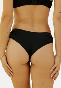 Bas de bikini noir avec une coupe haute et des panneaux latéraux ornés d'un motif léopard. Texture lisse, style ajusté.
