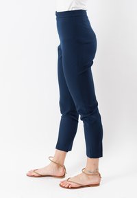 Pantaloni tailleur blu navy con vestibilità slim, tagliati alla caviglia, caratterizzati da una texture liscia e una vita piatta, abbinati a sandali con cinturini.