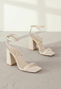 Beige Absatzsandalen mit Krokodilstruktur, quadratischer Zehenpartie und überkreuzten Knöchelriemen. Mit einem klobigen Blockabsatz.