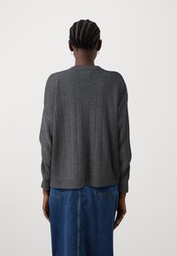 Grauer Strickpullover mit vertikaler Rippstruktur, Rundhalsausschnitt und überschnittenen Schultern, kombiniert mit einem blauen Jeansrock.