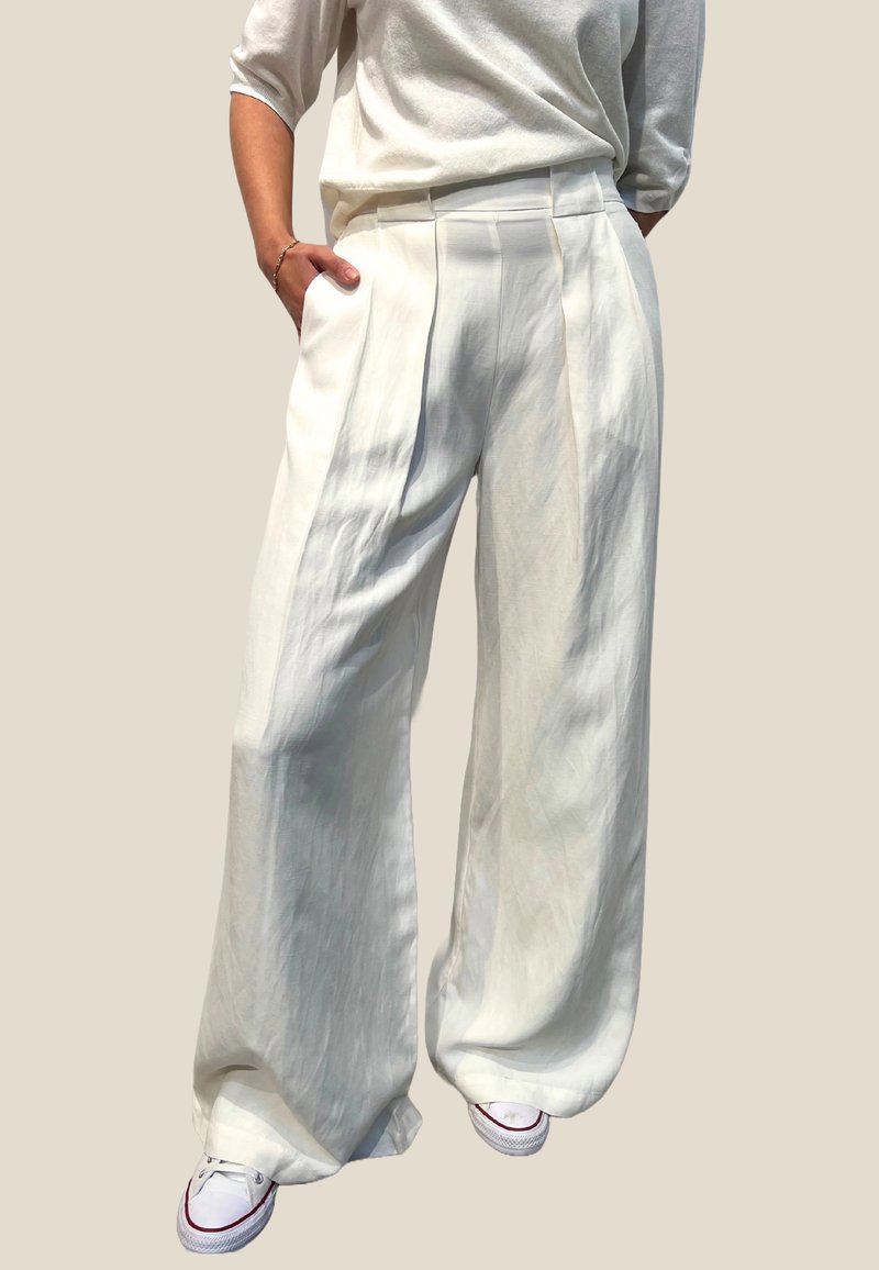 Vide benbukser i hvit lettvektig stoff med frontfolder og løs passform, kombinert med hvite sneakers.