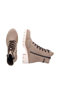 Bottines en suédine marron avec un laçage à l'avant, des zips sur le côté et des semelles en caoutchouc texturé blanc. Elles présentent un bout rond et des détails surpiqués.