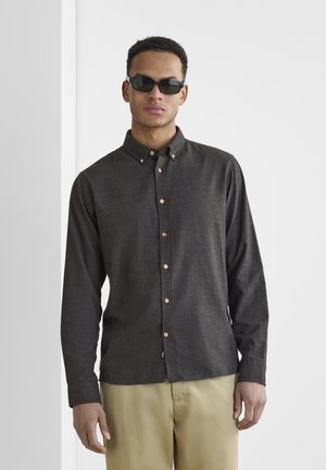 Dark button-up shirt with a collar, made of textured fabric. Features small gold buttons and long sleeves. Paired with light-colored trousers.