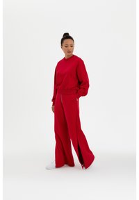 Roter Sweatshirt und passende weit geschnittene Hose mit Schlitzen. Hergestellt aus weichem Material; verfügt über gerippte Bündchen und ein gesticktes Logodetail.