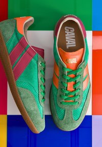 Paire de baskets en daim vert, orange et violet avec le logo "CAVAL", placées sur une surface à carreaux multicolore.