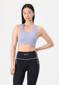 Light purple ribbed sports bra with a wide band and logo detail, paired with high-waisted black leggings featuring white accents.