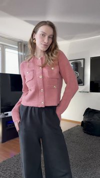 Rózsaszín kötött kardigán két első zsebbel és fényes gombokkal, laza fekete nadrággal párosítva. Puha tapintású és laza stílusú kialakítás.