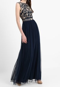 Mörkblå kvällsklänning med ärmlös, broderad bodice med blommönster och en flödande, genomskinlig kjol. Slät tyg med utsvängd design.