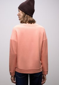 Różowa bluza o luźnym kroju z ściągaczami na rękawach. Noszona na ciemnych dżinsach, dopełniona brązową, prążkowaną czapką typu beanie. Prosty, schludny design.