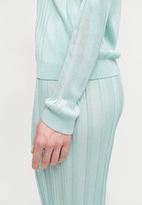 Πλεκτό σετ δύο τεμαχίων σε μέντα πράσινο χρώμα με ριμπ ύφανση, εφαρμοστή σχεδίαση και μακριά μανίκια με μανσέτες.