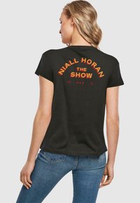 Sort bomulds T-shirt med rød og gul tekst: "NIALL HORAN THE SHOW LP3 23," buet design på ryggen. Korte ærmer, afslappet pasform.