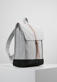 Harmaa kangaskauppareppu, jossa on läppä sulkeminen, pinkki nahkahihna, musta pohja ja säädettävät harmaat olkahihnat. Tasainen muotoilu.