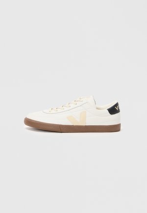 Sneaker bianco realizzato in materiale sintetico liscio, con un logo V beige, suola in gomma marrone chiaro e dettagli neri sul tallone.