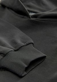 Un sweat à capuche noir avec des poignets côtelés et une texture douce. Le matériau semble lisse, avec un minimum de marques ou de motifs visibles.