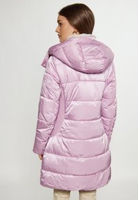 Palton pufos de culoare mov deschis cu glugă, cu un design quilted, textură netedă, buzunare laterale cu fermoar și căptușeală moale.