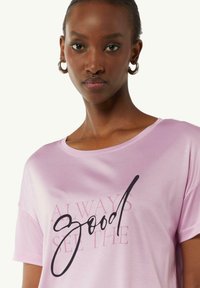Pink short-sleeve t-shirt with a loose fit, featuring black text that reads “always good” and subtle gradient background text. Smooth texture.