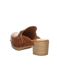 Sabot en cuir marron à dos ouvert, talon bloc en bois, bride à boucle en laiton et clous métalliques décoratifs le long du bord de la semelle.