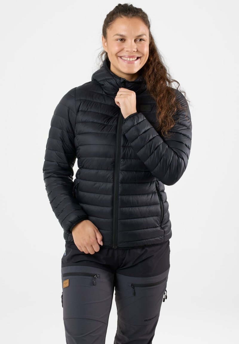Black padded jacket with a high collar, full zipper, slim fit, and side pockets. Worn over dark pants, featuring zippered pockets.