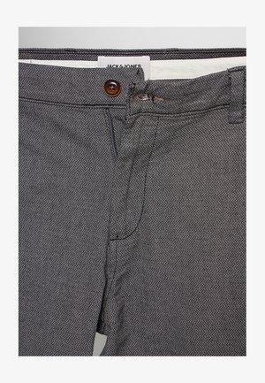 Grau strukturierte Hose mit Knopf- und Reißverschluss, zeigt Bunddetail und teilweise sichtbares weißes Innenfutter mit Markenlabel.