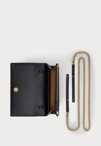 Melnas ādas rokassomiņa atveras uz brūnu iekšpusi, piedāvājot zelta krāsas pogu un rāvējslēdzēja aizdari. Ietver divas noņemamas siksnu opcijas: ķēde un āda.