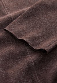 Tissu en tricot marron avec une texture côtelée et un bord ondulé sur la manche. Le matériau semble doux et confortable.