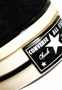 Scarpa Converse Chuck Taylor nera con texture pelosa, suola in gomma bianca e etichetta nera con il nome del marchio e il logo a stella.