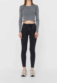 Grå randig kort topp med långa ärmar, kombinerad med höga svarta skinny jeans med framsidiga dragkedjor och beige sneakers.